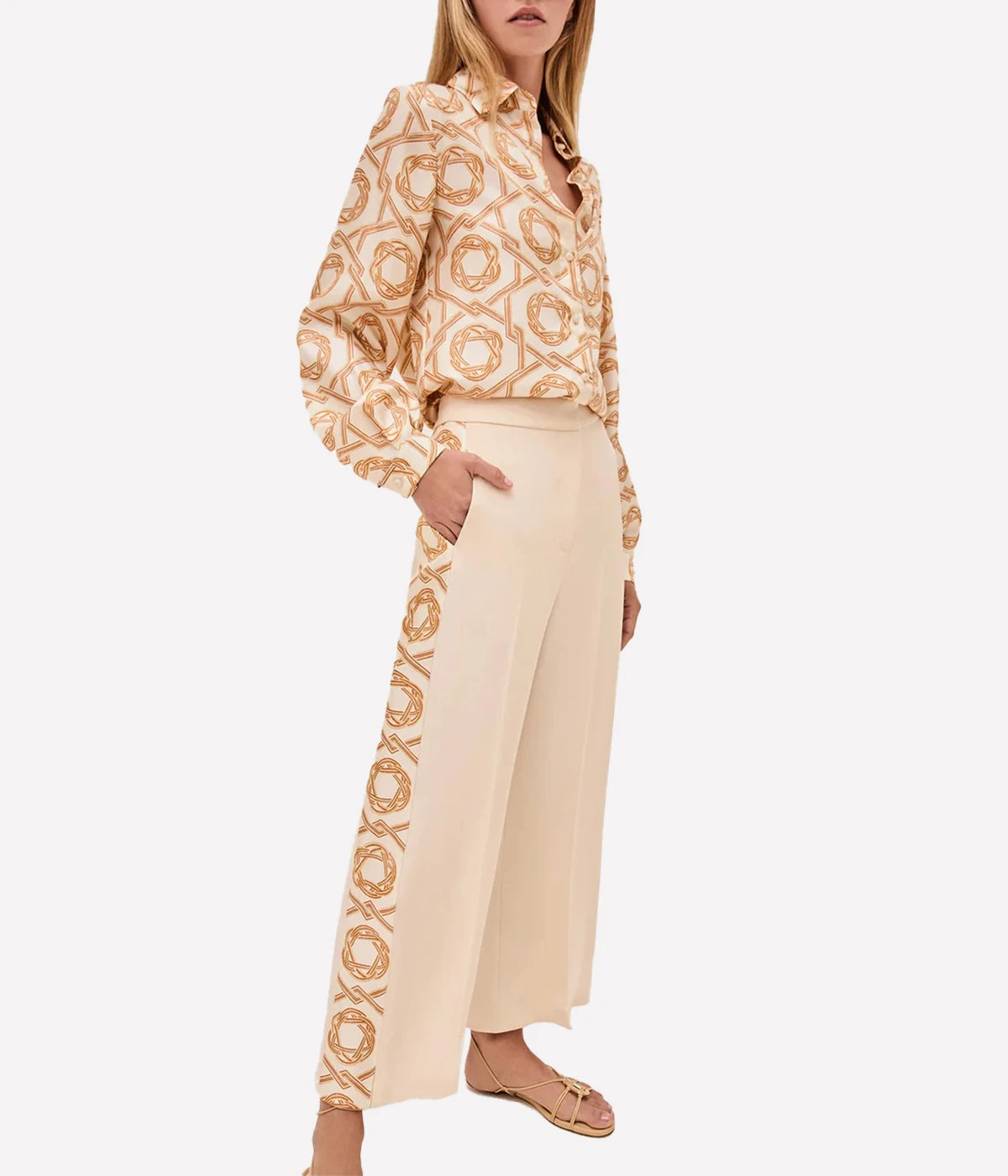 Orange and cream printed button-up blouse with shirt collar and cuffed sleeves, styled with high-waisted trousers.