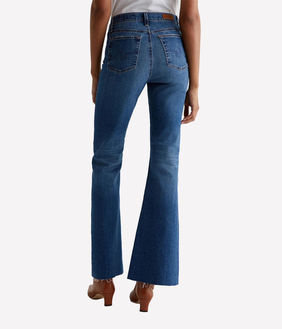 A pair of Madi high-rise flare jeans from AG in dark indigo wash with fading, whiskering, and raw hems. The jeans feature a high-rise waist and flare from the knee down, with a flattering fit through the hips.